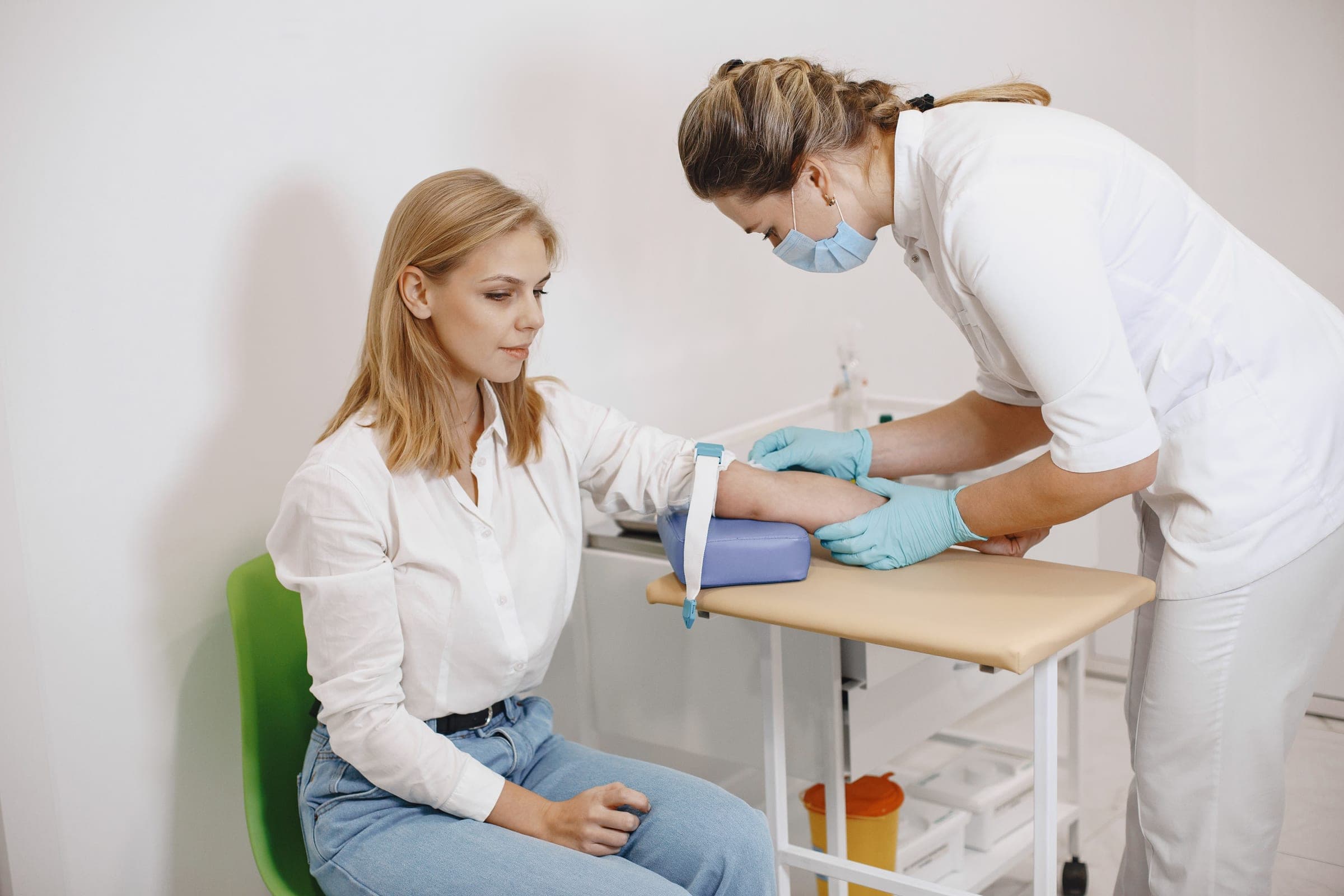 A nurse performs a blood test on a seated female patient in a medical setting