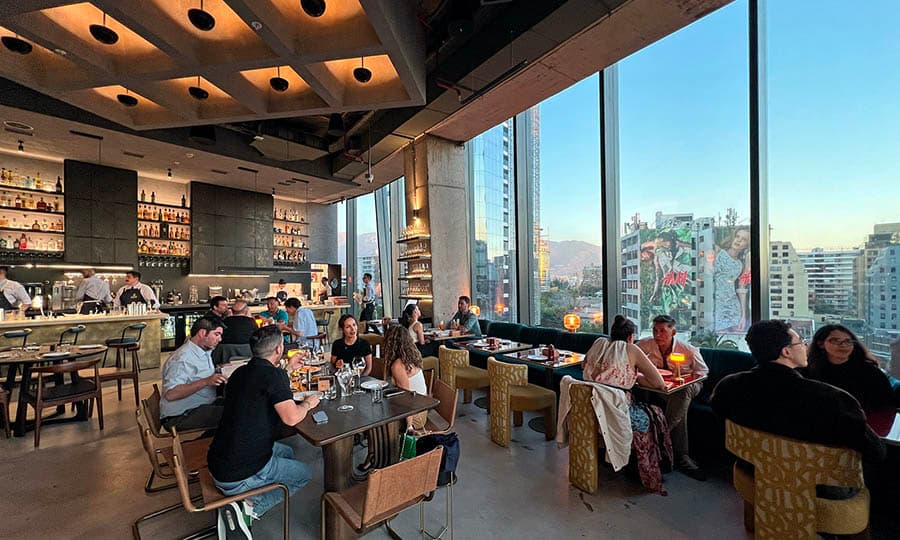 A bustling new restaurant in Santiago, tables filled with diners enjoying their food with a city skyline backdrop